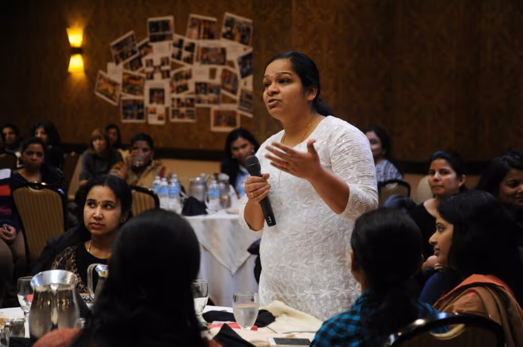 woman stands in a room full of people, microphone in hand to share an opinion