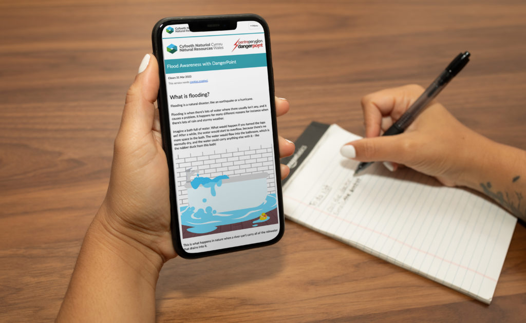 Close up of someone looking at information about flooding on a phone in one hand while writing notes with the other