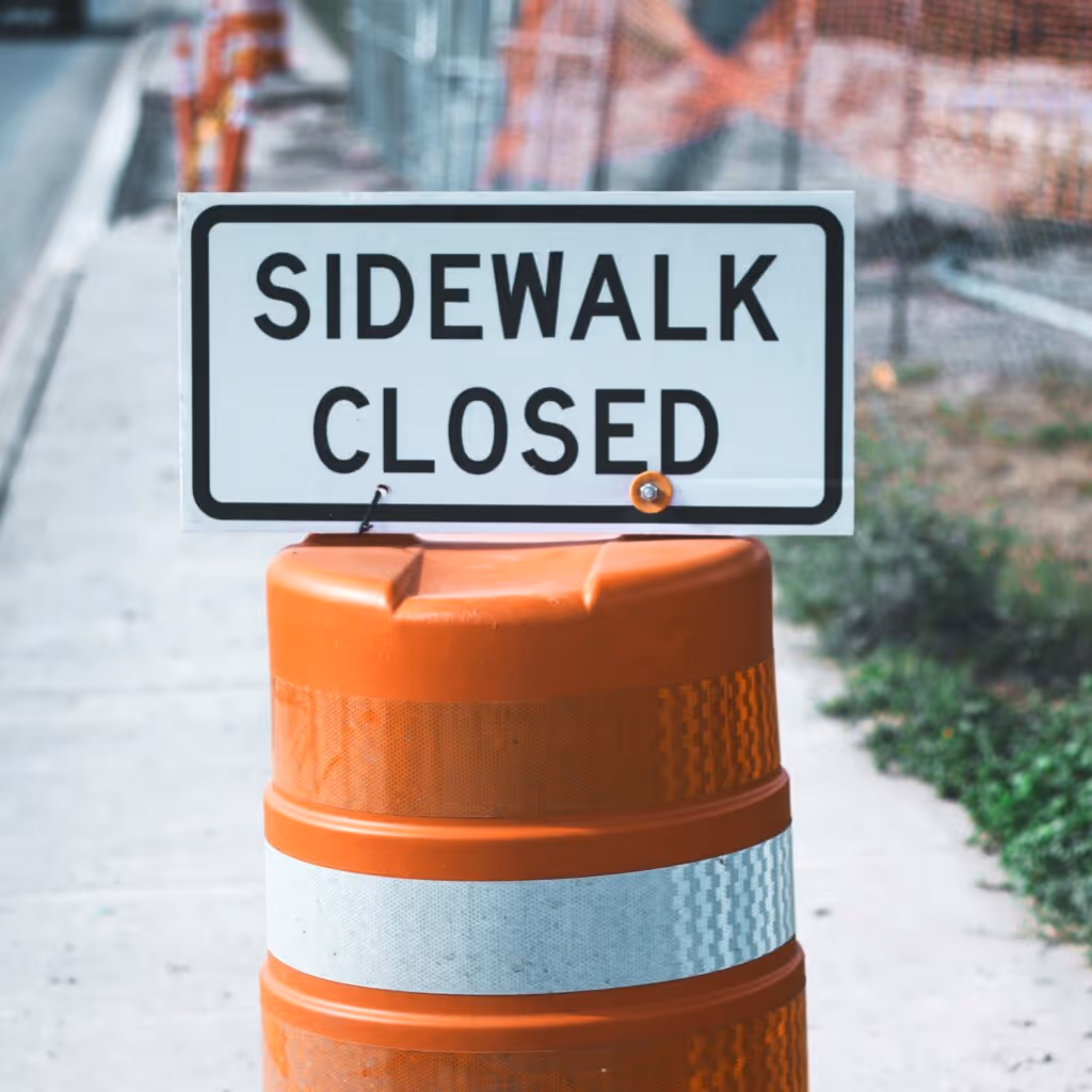 Image of a closed sidewalk with an orange bollard.