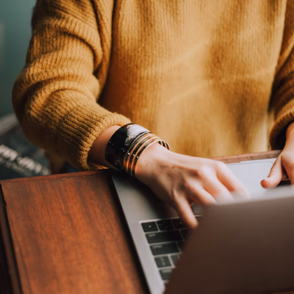 A person in a yellow sweater typing on a laptop.