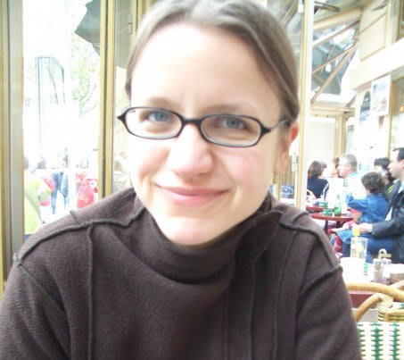 Fran Bennett, with hair tied back and glasses smiles at camera