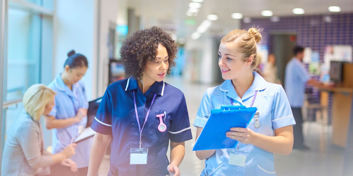 two nurses stand talking in a corridor