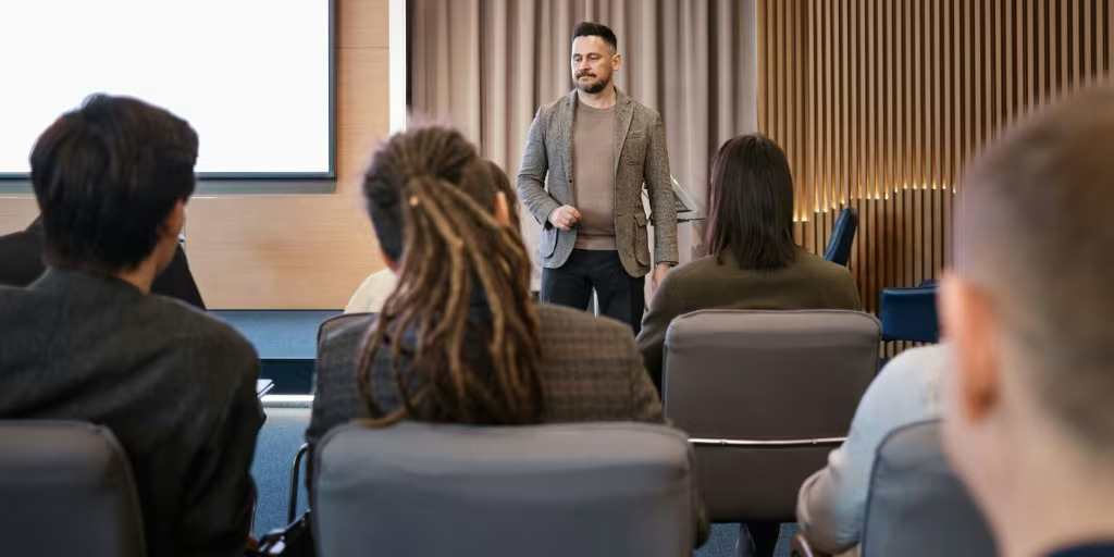 man stands in front of a group of seated people giving a speech