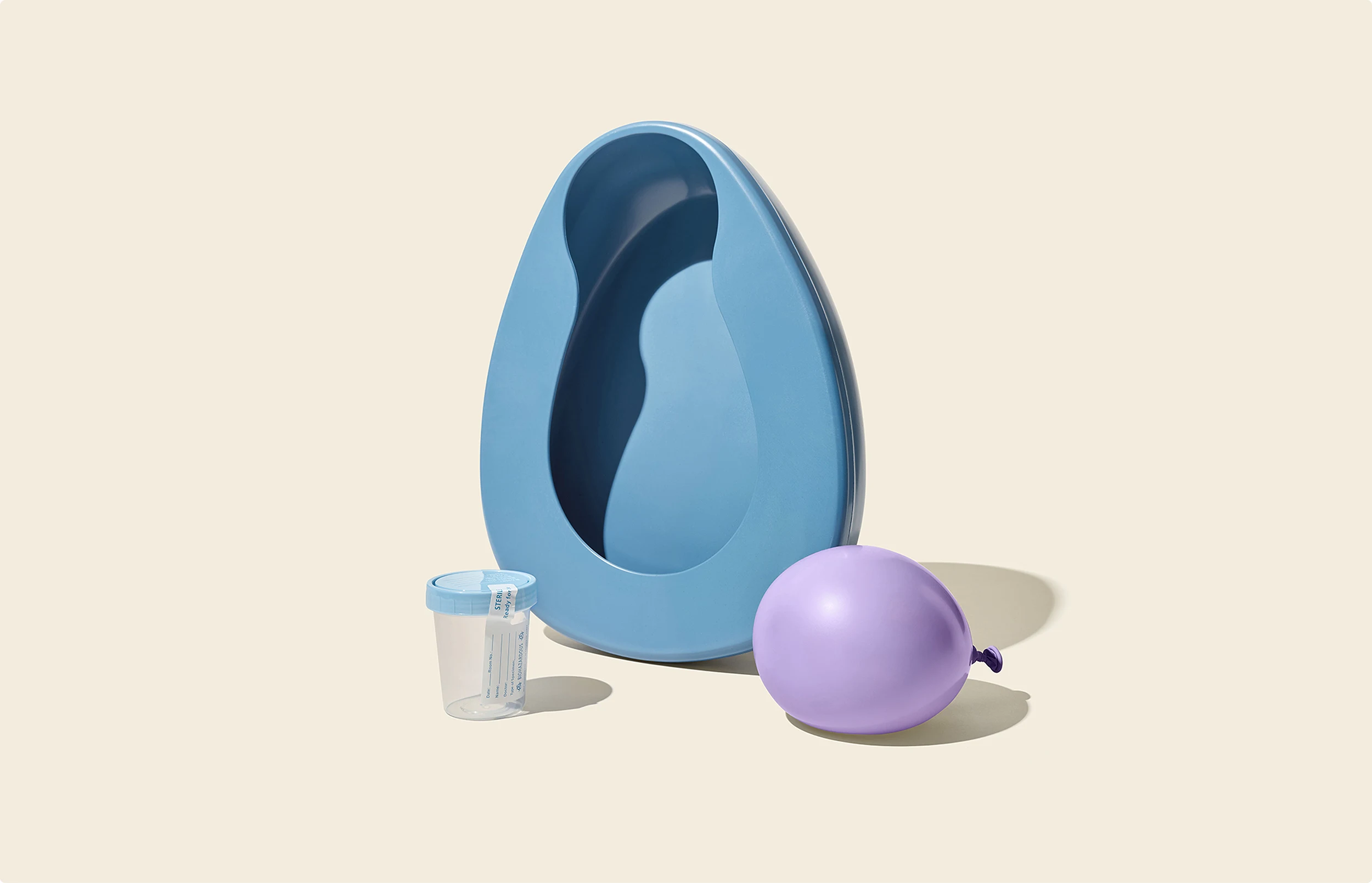 A beautifully designed photograph of a bed pan, sample cup and water balloon set against a cream background. This is a brand element created for athenahealth by Colossus Creative Co.
