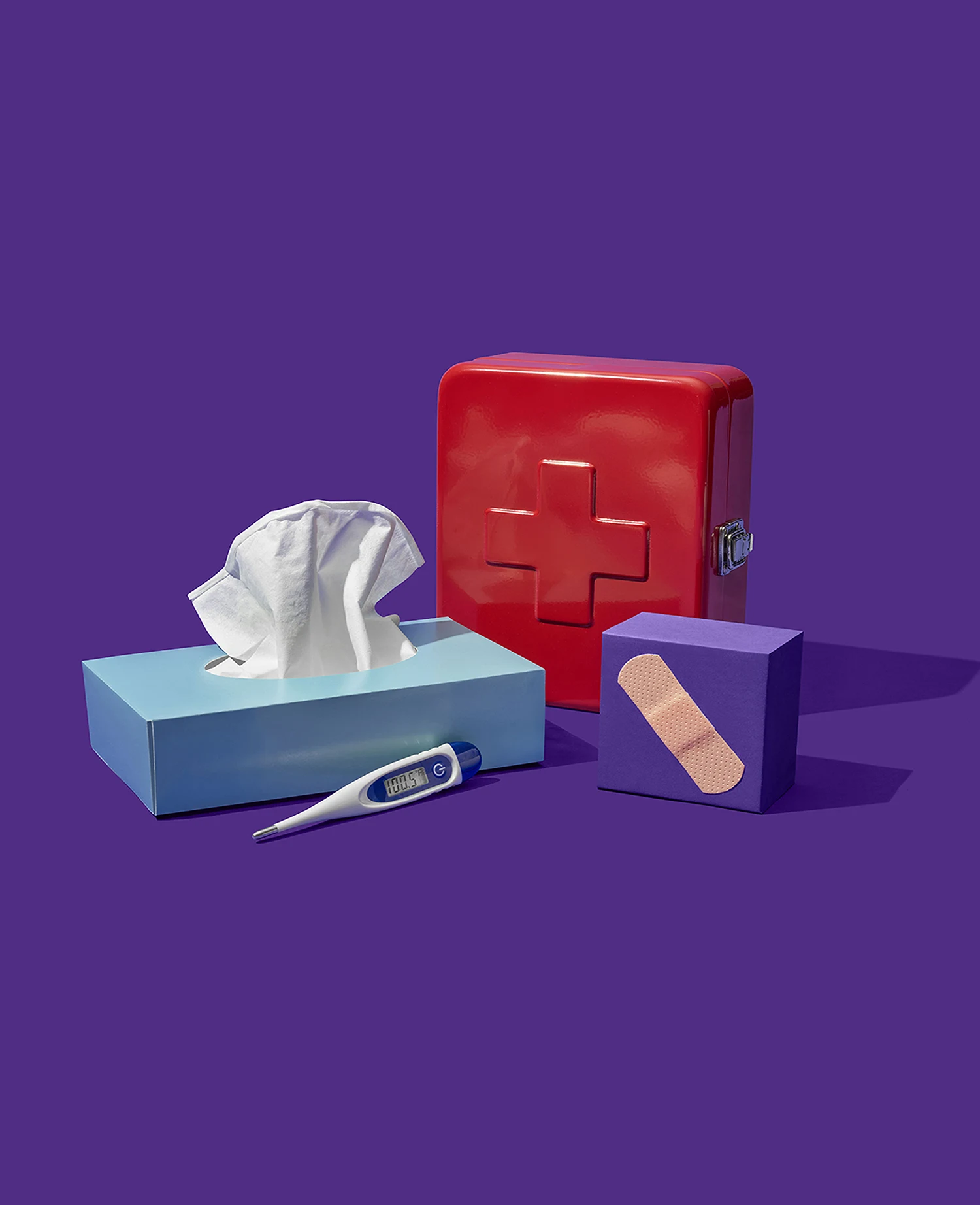 A beautifully designed photograph of a tissue box, first aid kit, bandaid and thermometer set against a purple background. This is a brand element created for athenahealth by Colossus Creative Co.