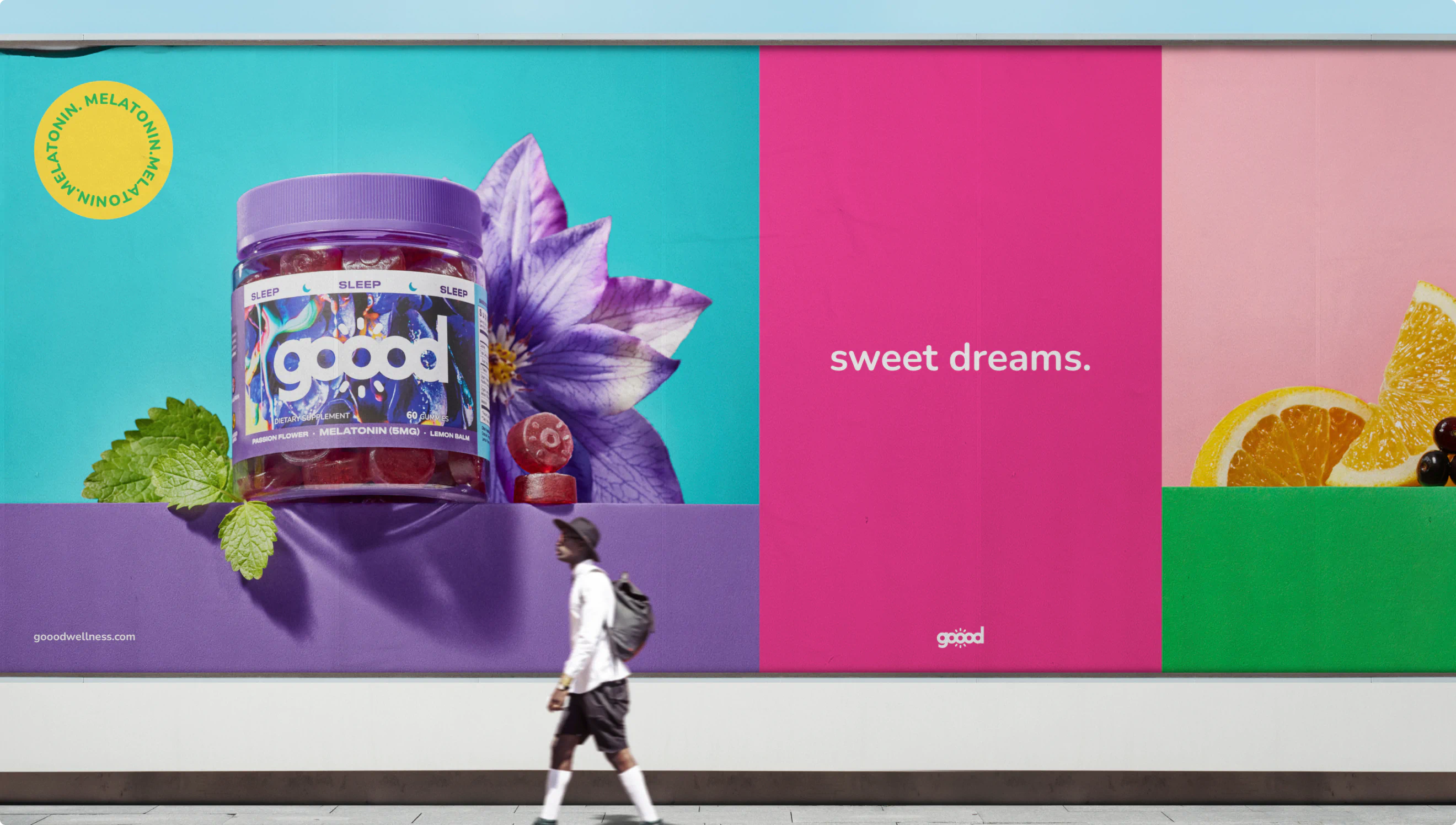 A man walks past a large billboard in a downtown area advertising Goood Wellness melatonin. The copy reads "sweet dreams."