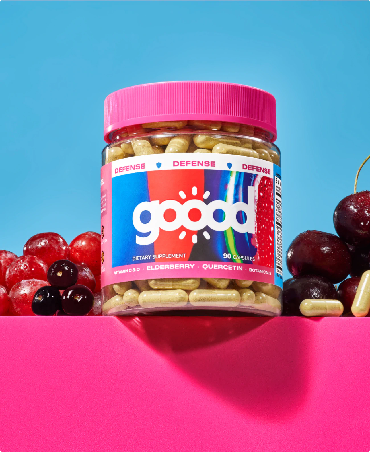 A single bottle of Goood Wellness supplements on a pink surface, surrounded by cherries and grapes.