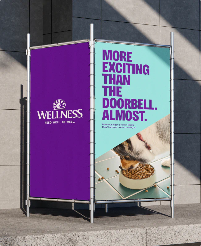 A clever outdoor ad for Wellness Pet Company. We see an Australian Cattle Dog eating a bowl of food with the headline: "More exciting than the doorbell. Almost."