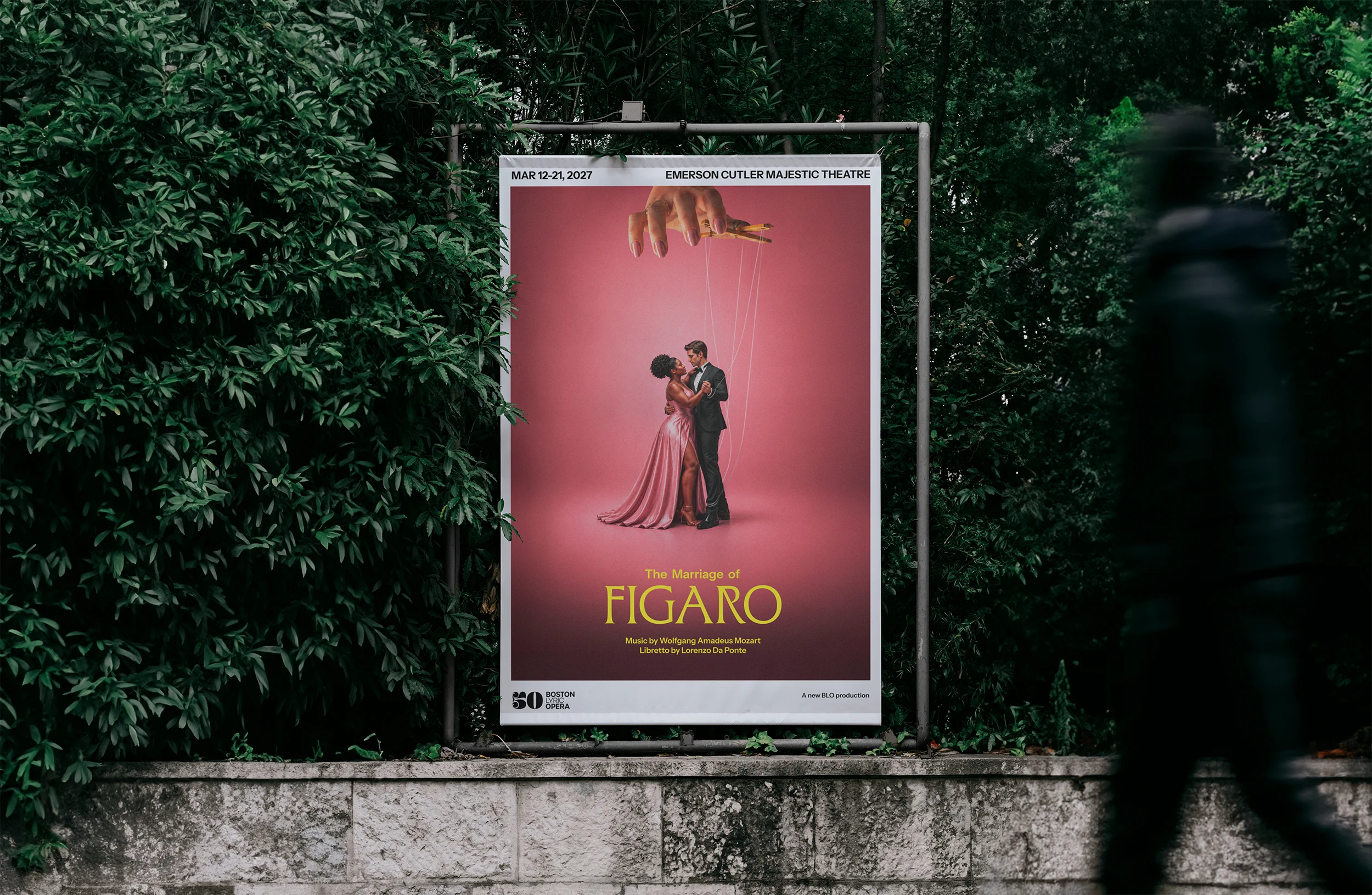 Outdoor poster and billboard for "The Marriage of Figaro" from Boston Lyric Opera featuring a man and woman dancing while being controlled by an omnipotent puppet master.