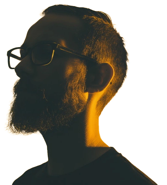 Silhouetted profile of a bearded man wearing glasses, dramatically lit from behind with a strong yellow-orange backlight.