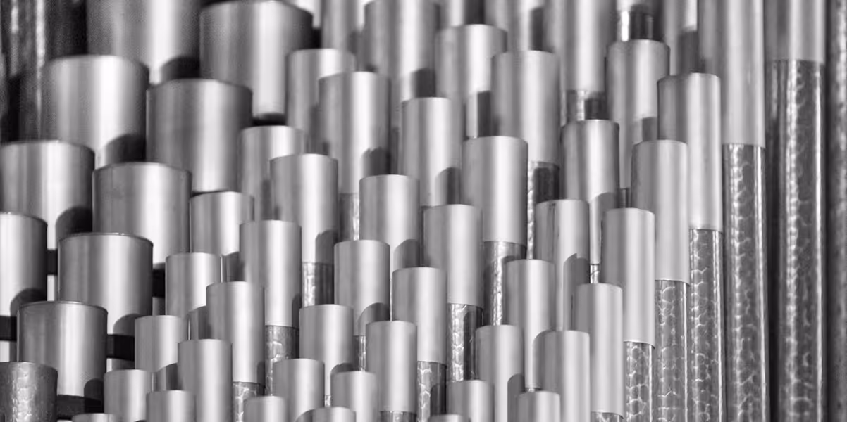 A black-and-white image of metal tubes arranged in rows, varying in size, creating an abstract pattern.