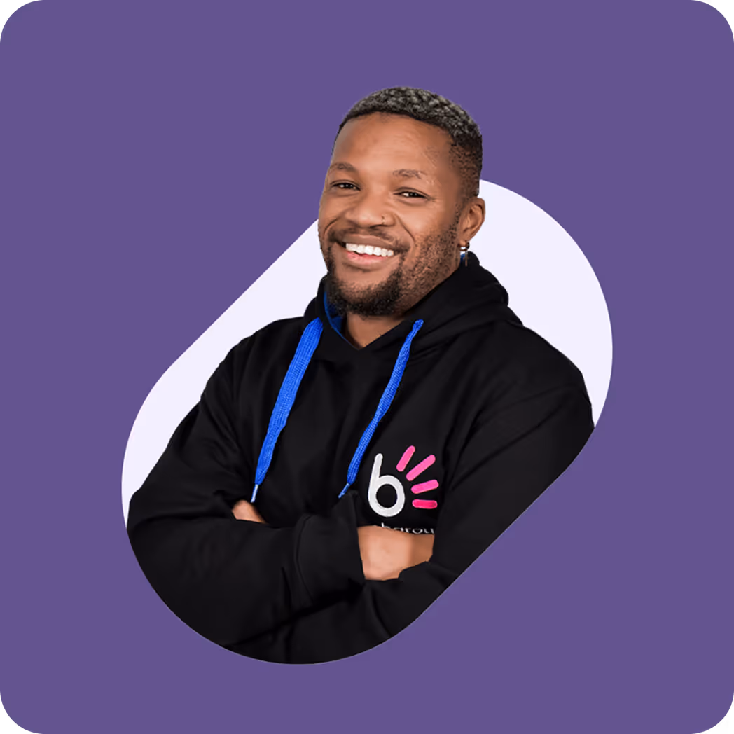Smiling man in a black Bob.co.za hoodie with arms crossed, standing against a purple background.