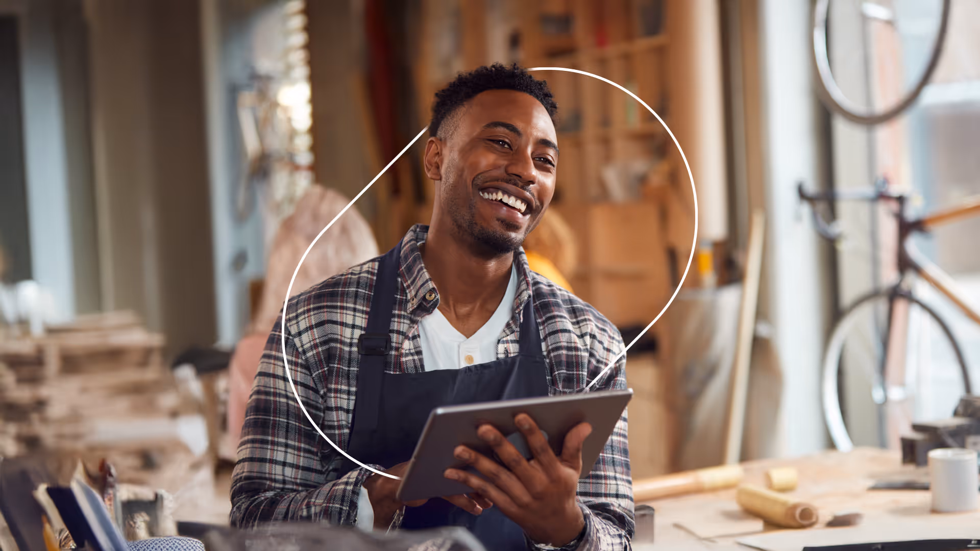 Smiling small business owner using a tablet in a workshop, surrounded by tools and a bicycle in the background.
