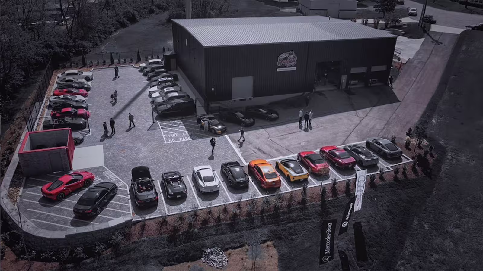 Aerial view of Cooper’s Garage in Franklin, Tennessee, showing the shop building, customer parking lot filled with European cars, and branded service flags for Mercedes-Benz, Audi, and Volkswagen.