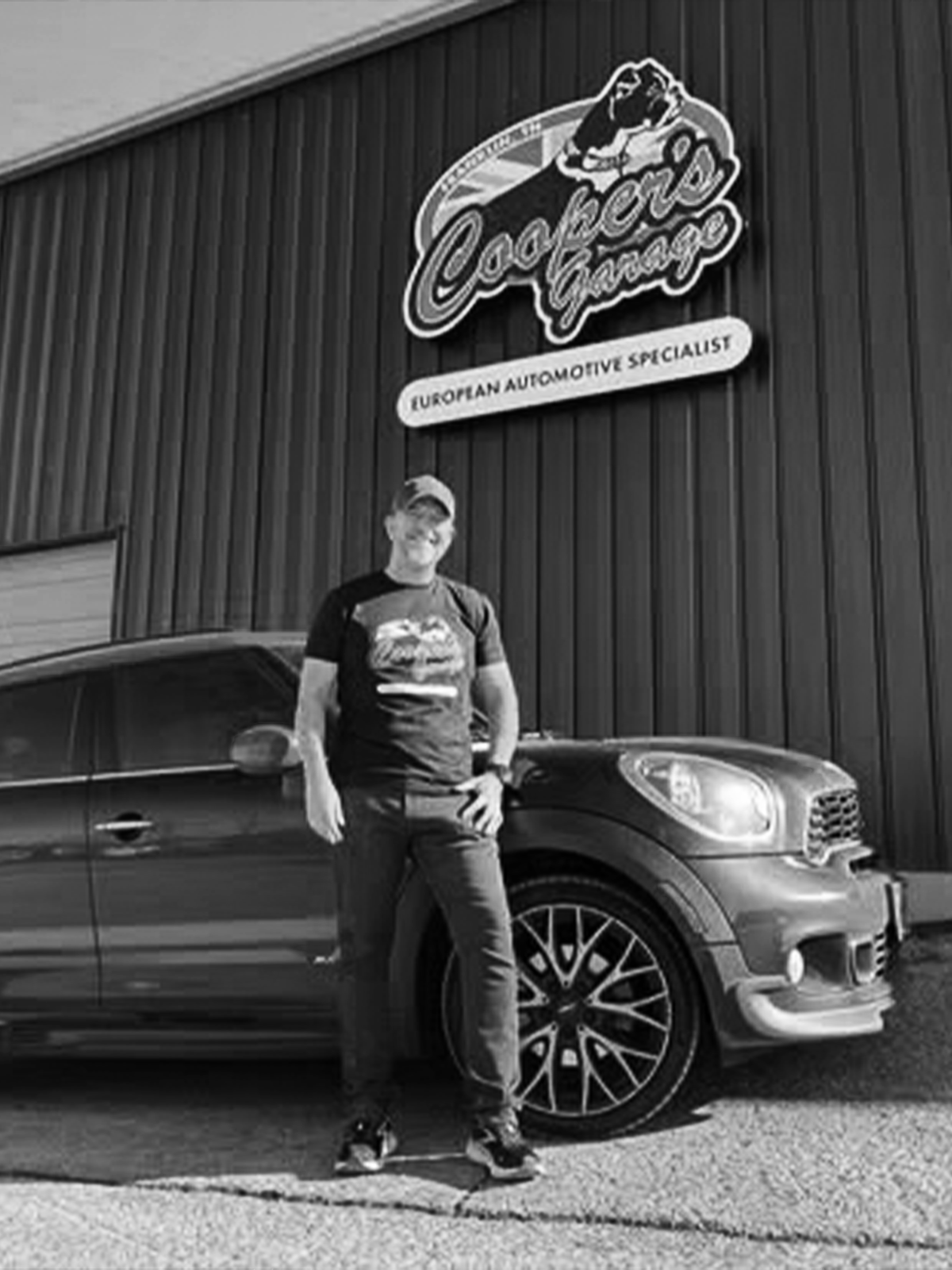 Customer standing proudly next to a MINI outside Cooper’s Garage, with the shop’s European automotive specialist sign visible in the background.