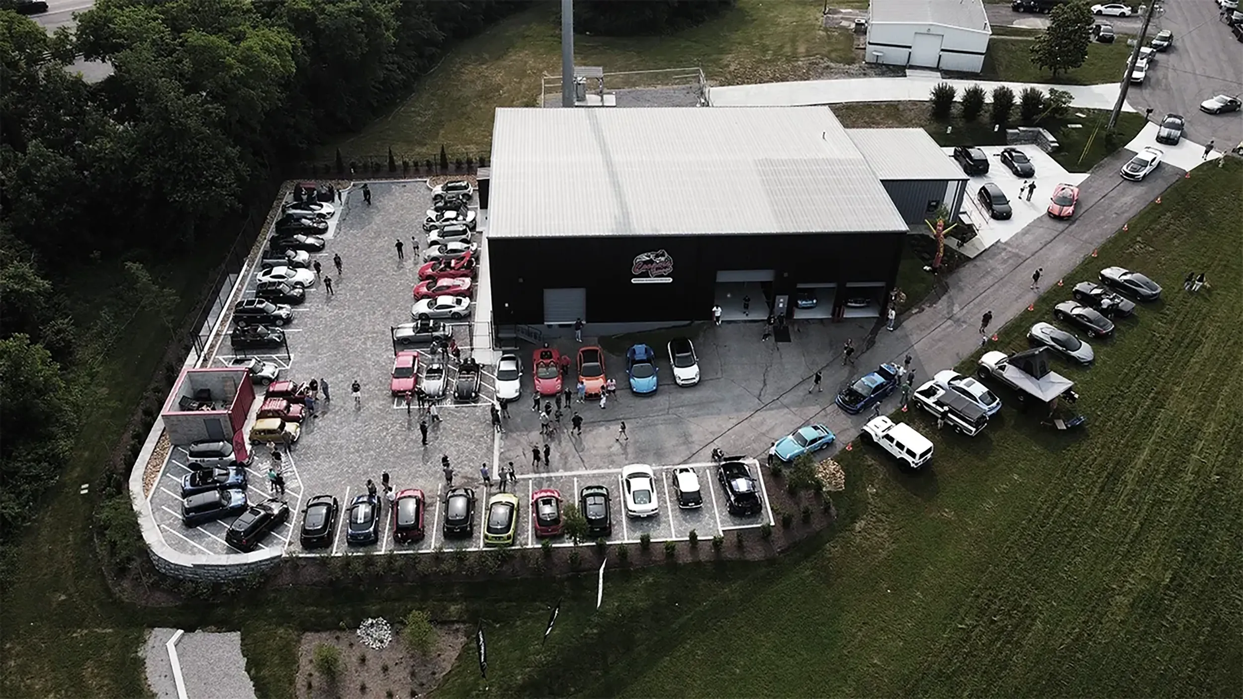 Aerial view of a Cars & Coffee event at Cooper’s Garage, with a large turnout of European vehicles and guests filling the parking lot and surrounding areas.