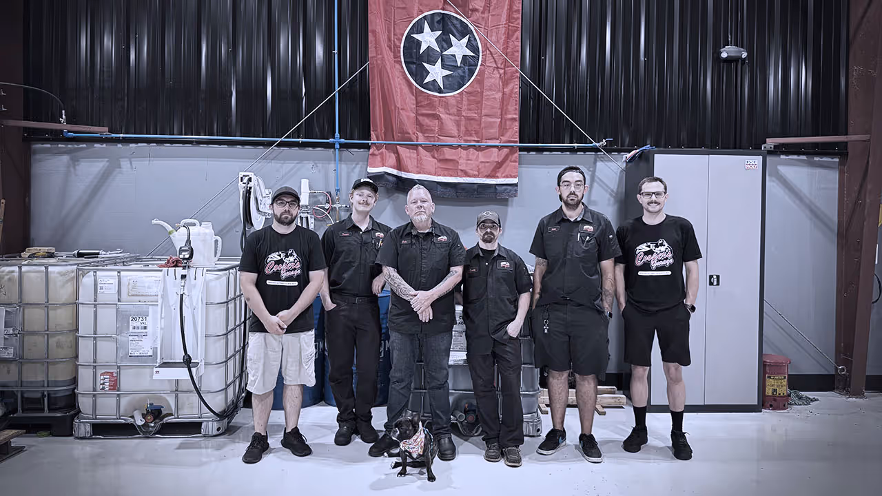 The Cooper’s Garage team standing together inside the shop beneath a Tennessee flag, with a small dog front and center.