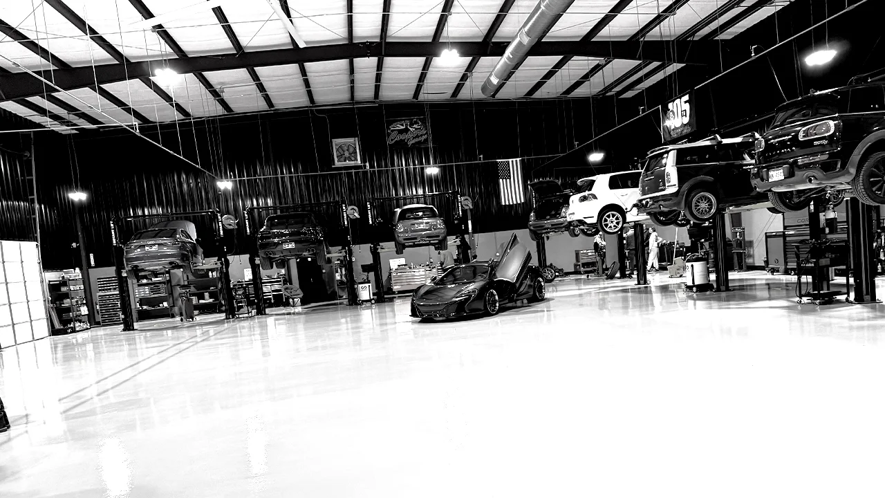 Cooper’s Garage service bay with European cars on lifts and McLaren in center