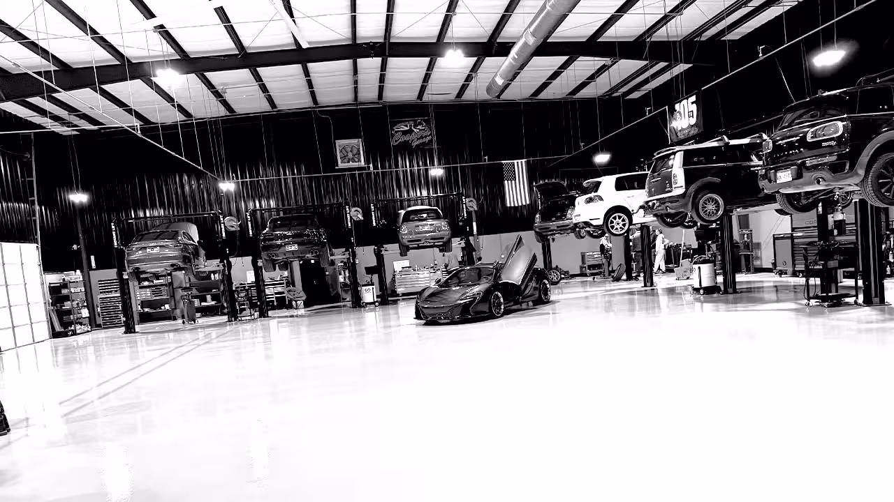 Cooper’s Garage service bay with European cars on lifts and McLaren in center