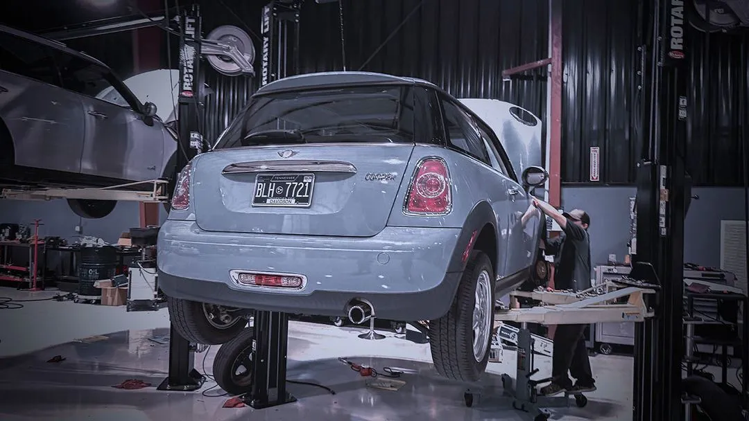 Technician working on a MINI Cooper raised on a lift at Cooper’s Garage service bay

