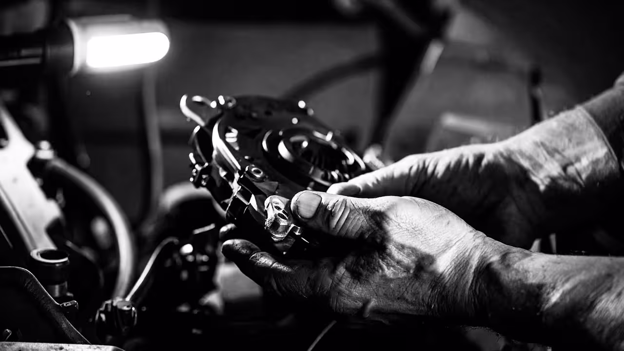 Mechanic holding clutch assembly under hood with visible hand tools and light — Cooper’s Garage clutch pedal and master cylinder service for European vehicles.