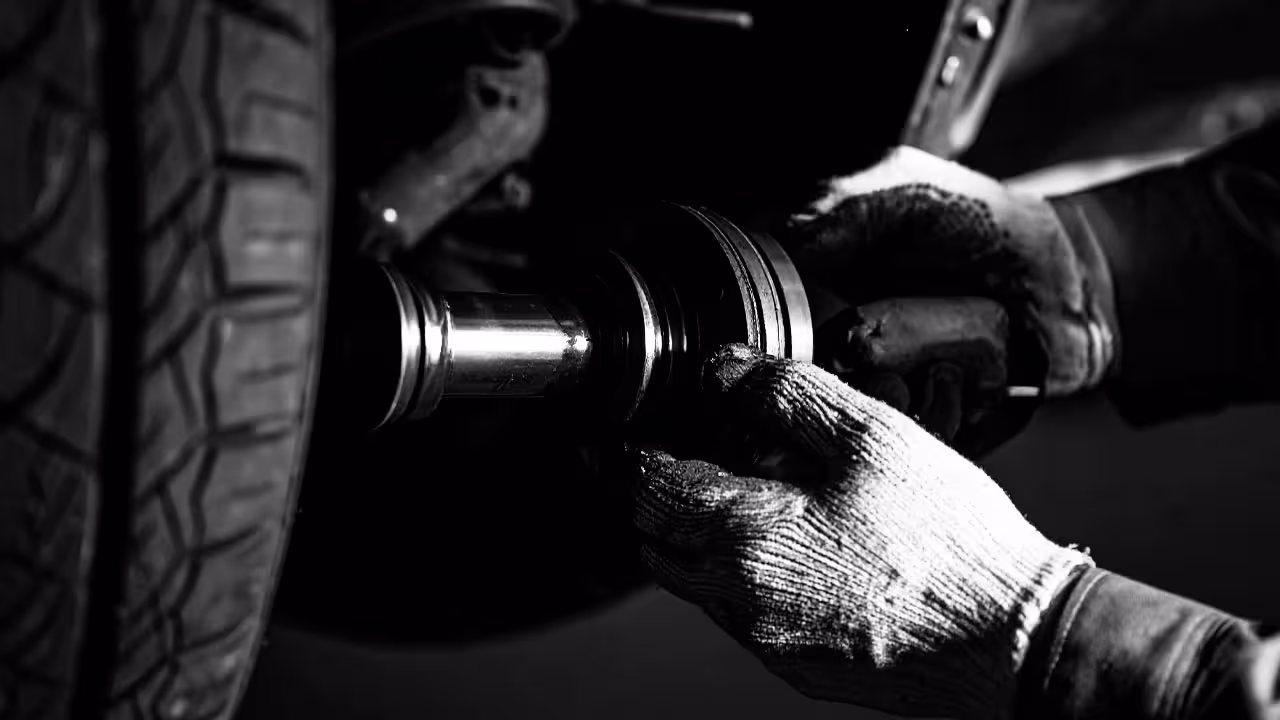 Technician inspecting driveshaft and flex disc near wheel hub — Cooper’s Garage driveshaft and flex disc inspection for vibration issues and drivetrain wear on European vehicles.