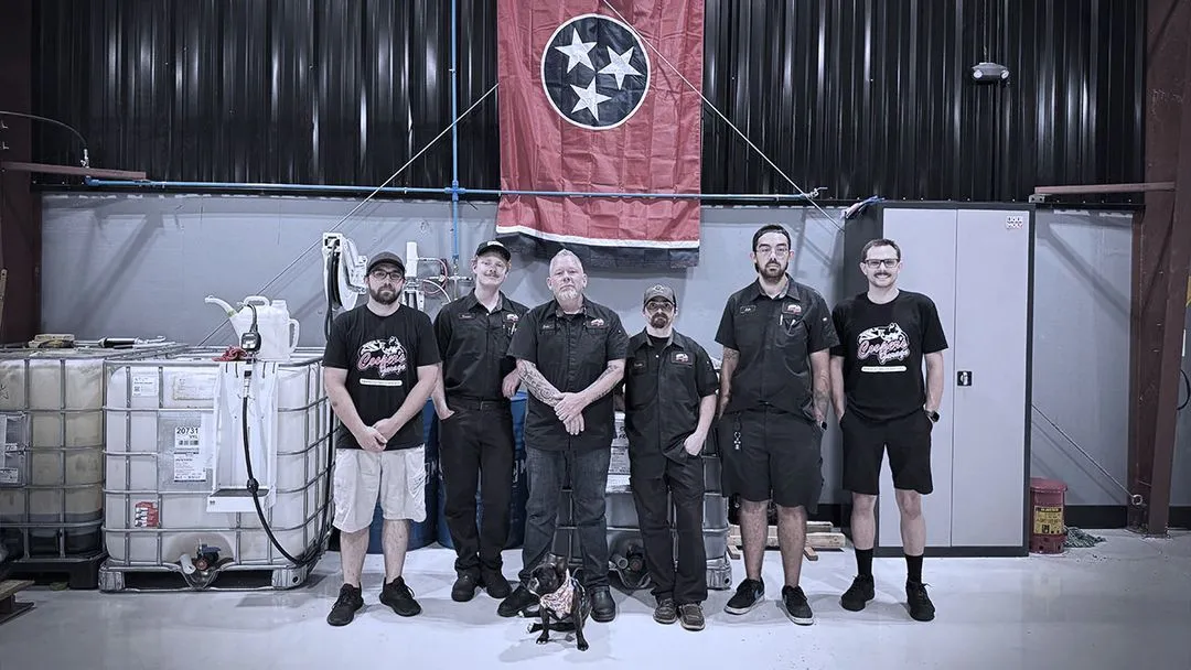 Cooper’s Garage team standing in front of equipment and a Tennessee state flag inside the shop