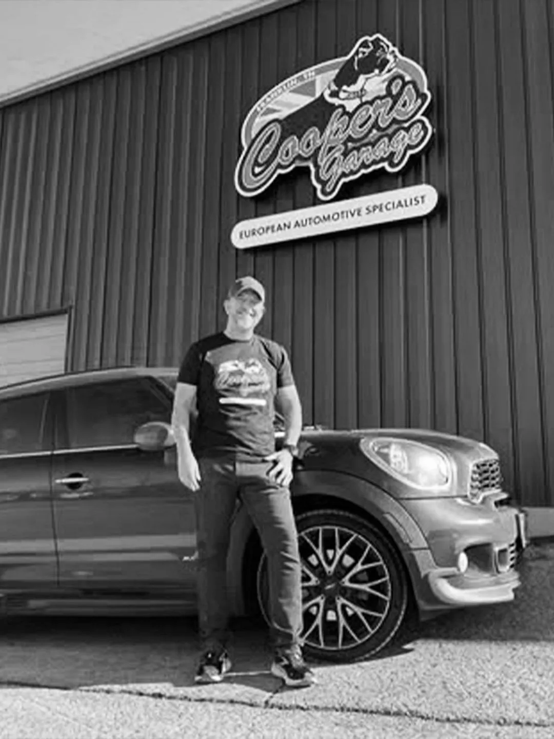 Customer standing next to a MINI Cooper in front of the Cooper’s Garage building and logo