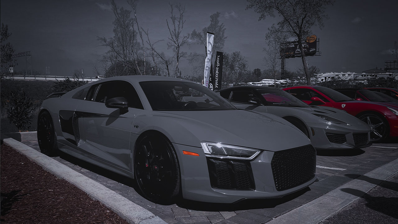 Gray Audi R8 parked at a Cooper’s Garage event alongside other high-performance European sports cars, including models from Lotus and Ferrari.

