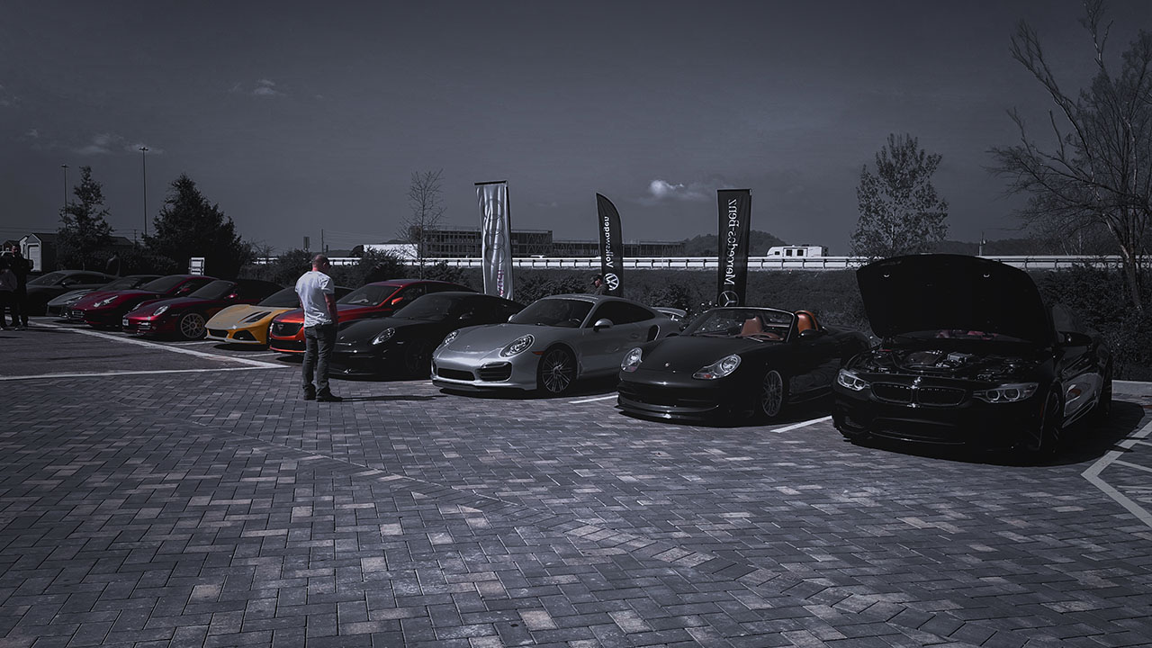Lineup of high-performance European vehicles including Porsche, Ferrari, and BMW at a Cooper’s Garage Cars & Coffee event, with branded flags in the background.