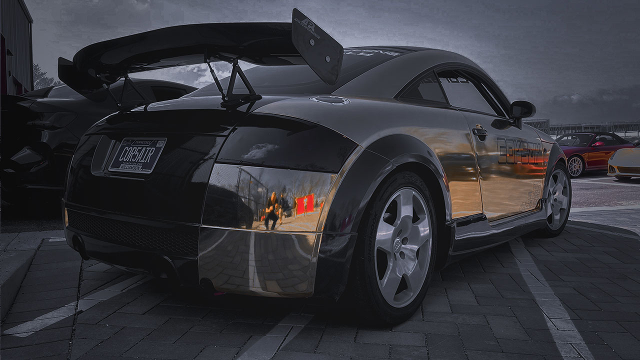Custom chrome-wrapped Audi TT with large rear wing and “CORSAIR” Tennessee license plate, parked at a Cooper’s Garage event alongside other European performance cars.

