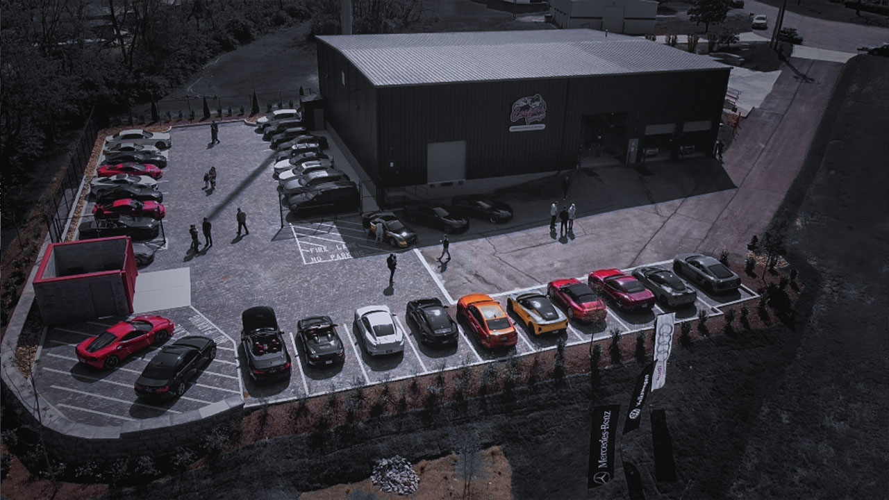 Aerial view of Cooper’s Garage during an event, with rows of European sports cars and guests gathered across the parking lot on a clear day.

