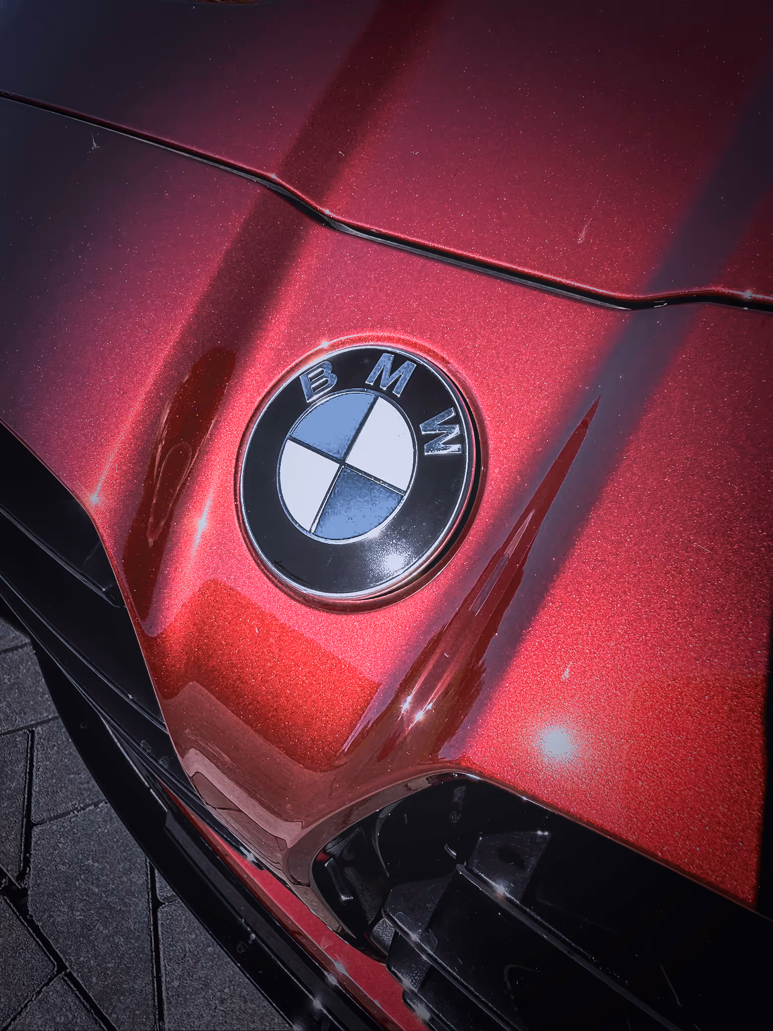 Close-up of a red BMW car hood showing the BMW roundel emblem in sunlight.