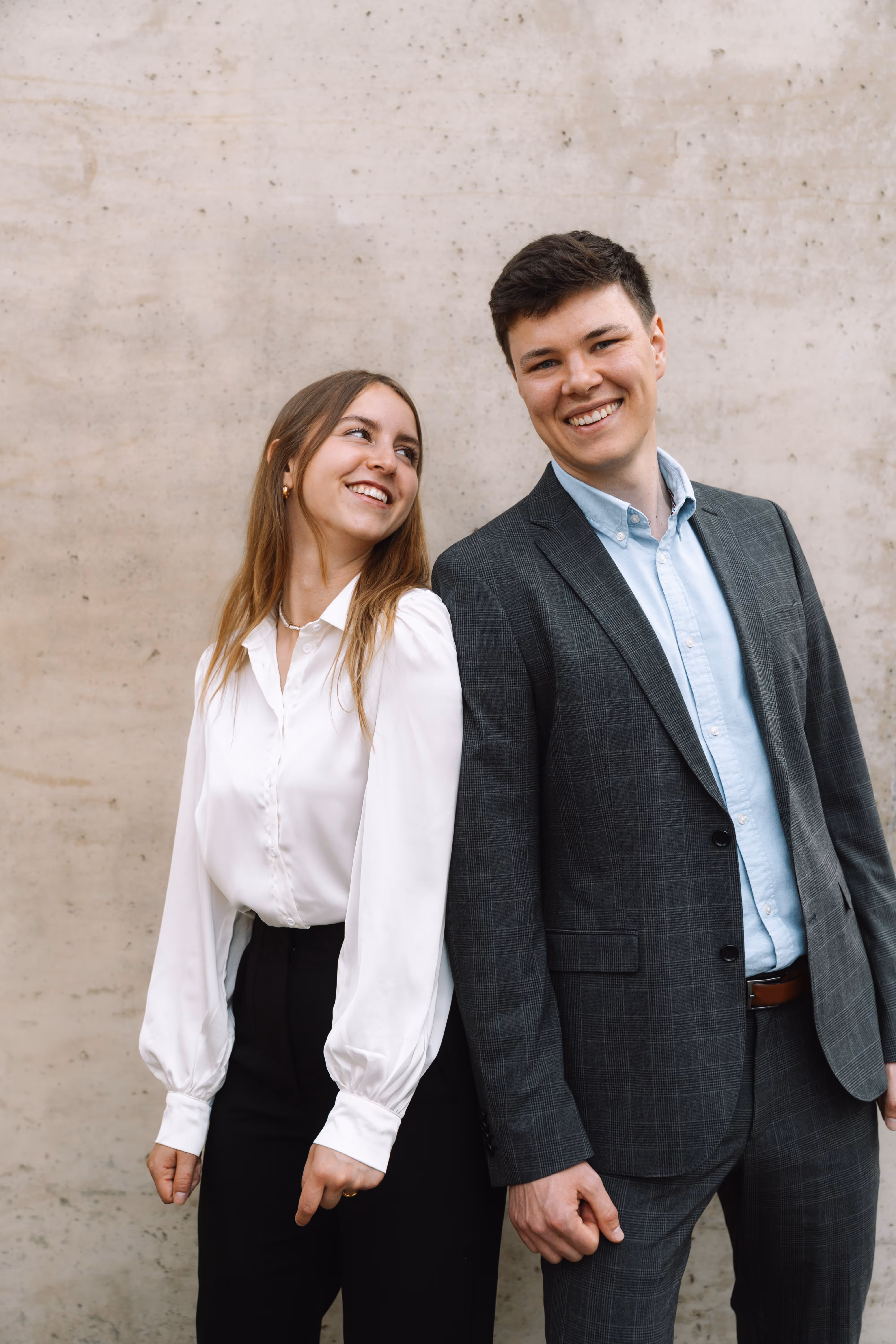 Die zwei Gründer von vimaso stehen nebeneinander vor einer hellen Wand, lächeln und blicken sich an.