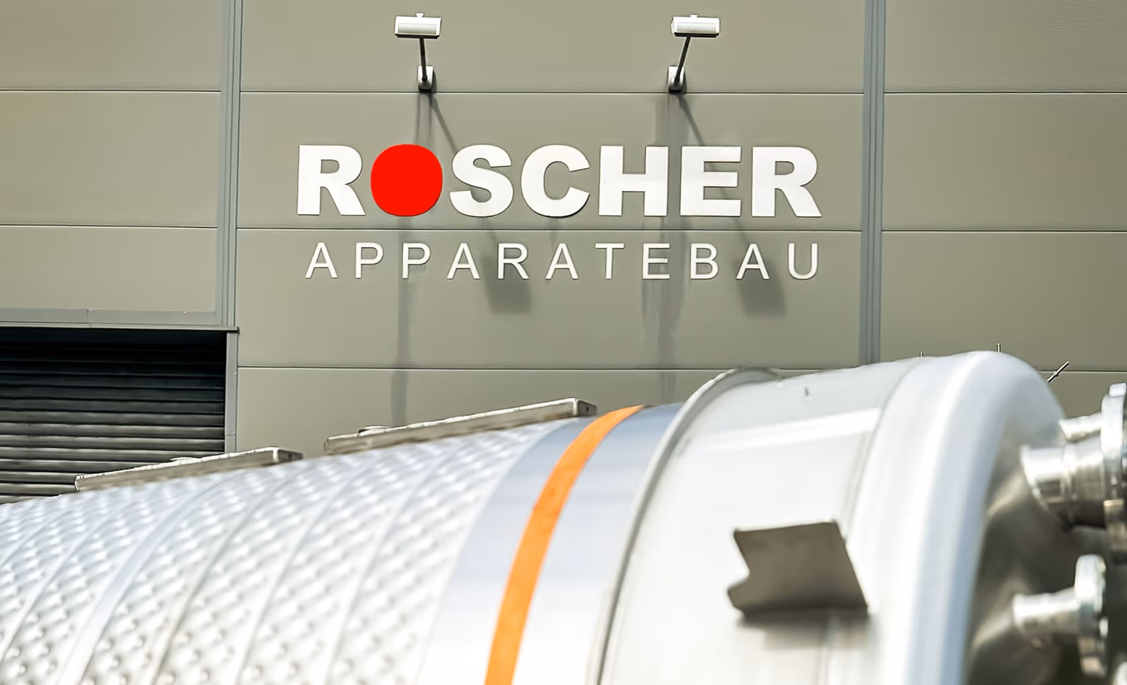 Ein Edelstahltank vor einer Halle mit der Aufschrift Roscher Apparatebau
