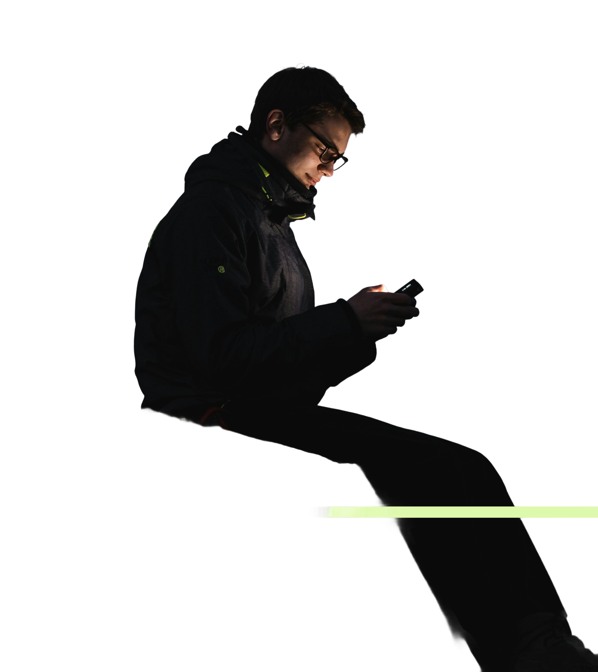 Jeune homme portant des lunettes regardant son téléphone dans l'obscurité avec un léger halo lumineux autour.