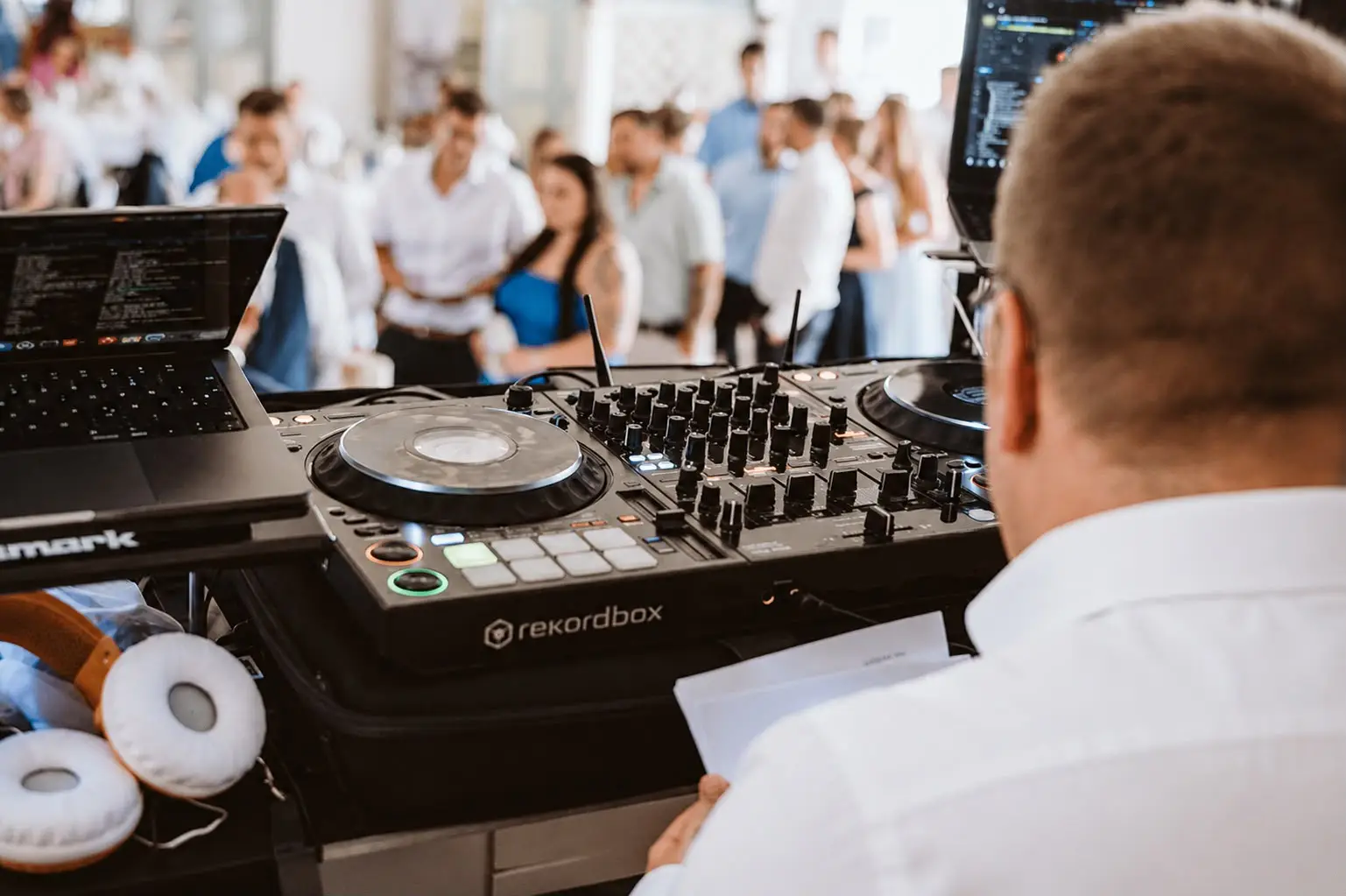 DJ bedient ein Mischpult und Laptop vor einer Menge auf einer Veranstaltung.