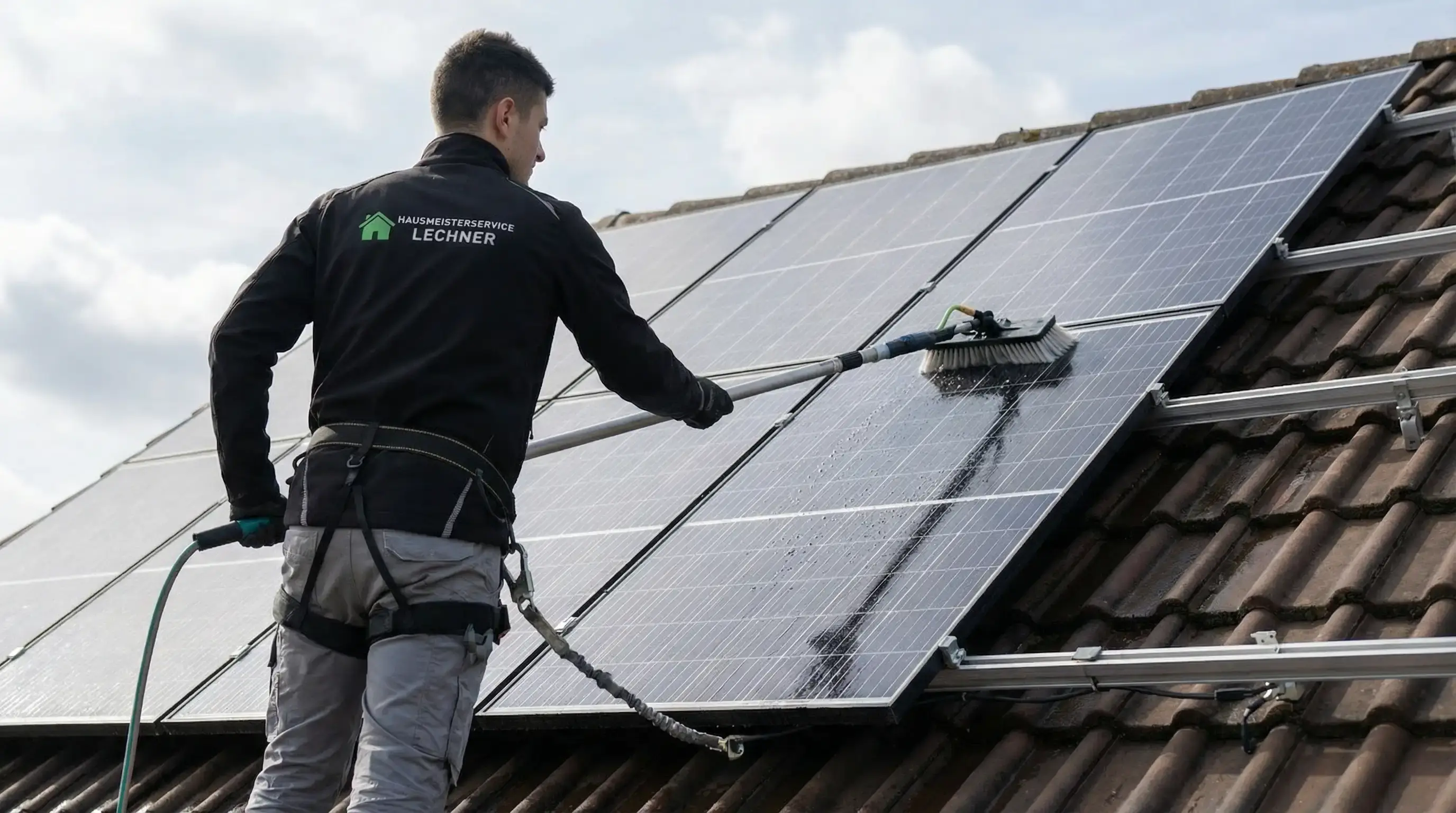 Mann reinigt Solarpaneele auf einem Dach mit einer Bürste und Wasser.