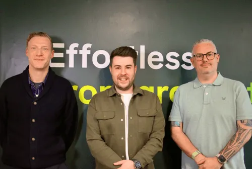 Three men standing in front of a wall with partially visible text in the background.