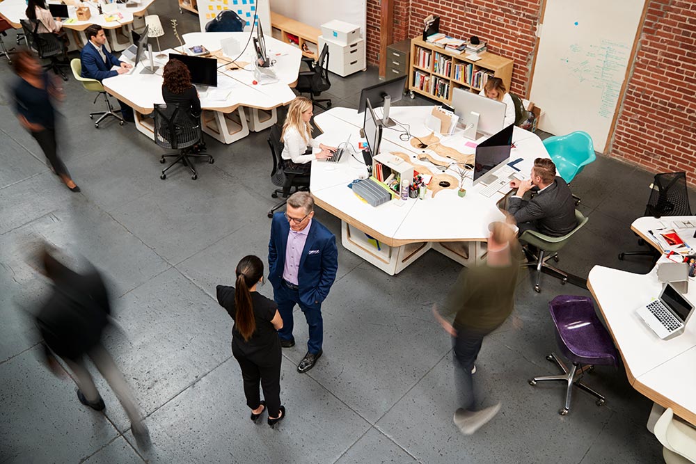 Overhead view of a busy modern open-plan office with people working at desks and some walking around.