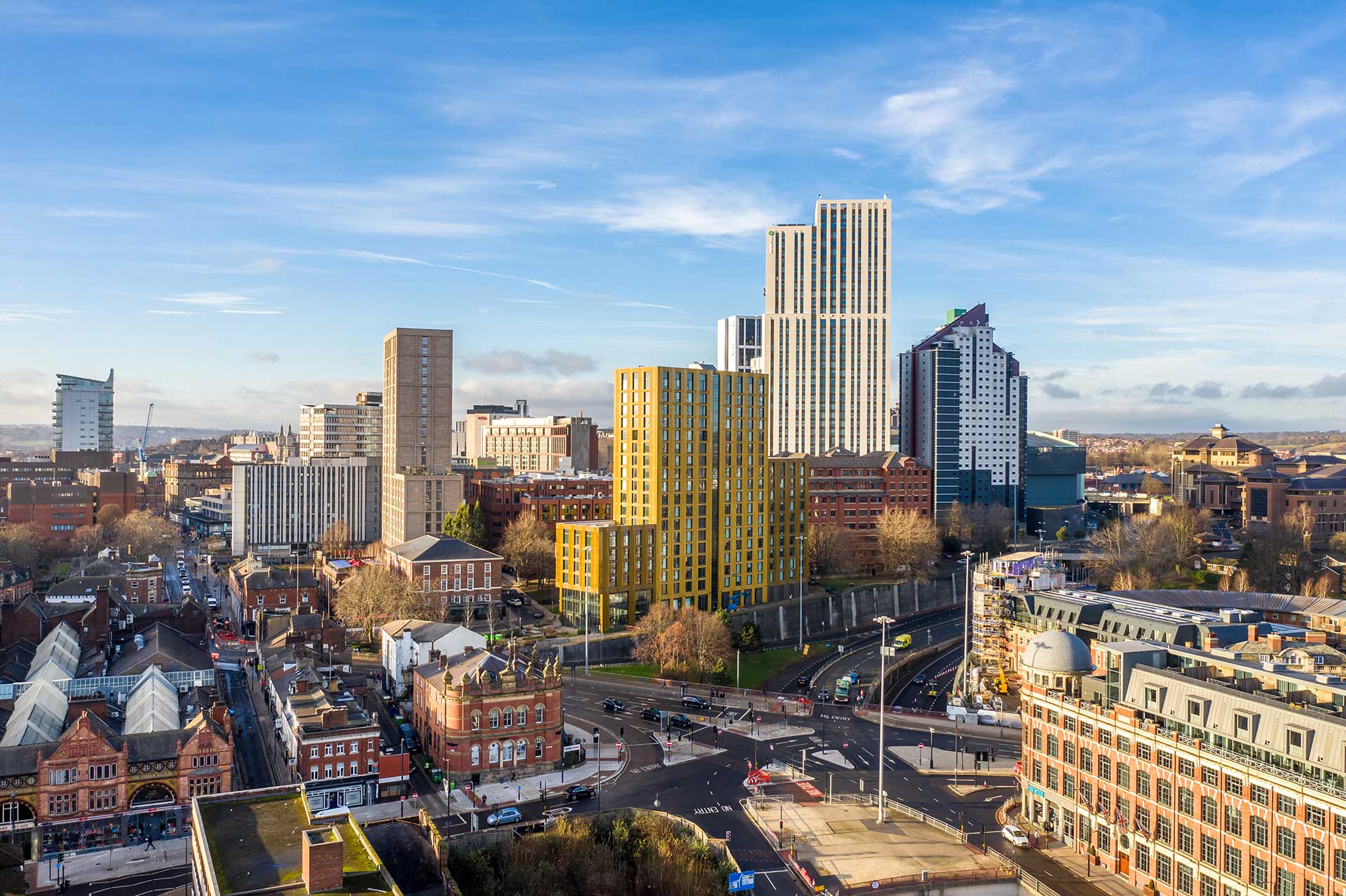 Cityscape of Leeds featuring modern and historic buildings under a blue sky.