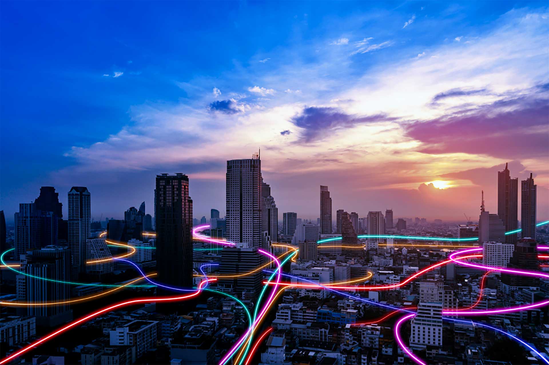 City skyline at sunset with colorful neon light trails weaving through buildings.