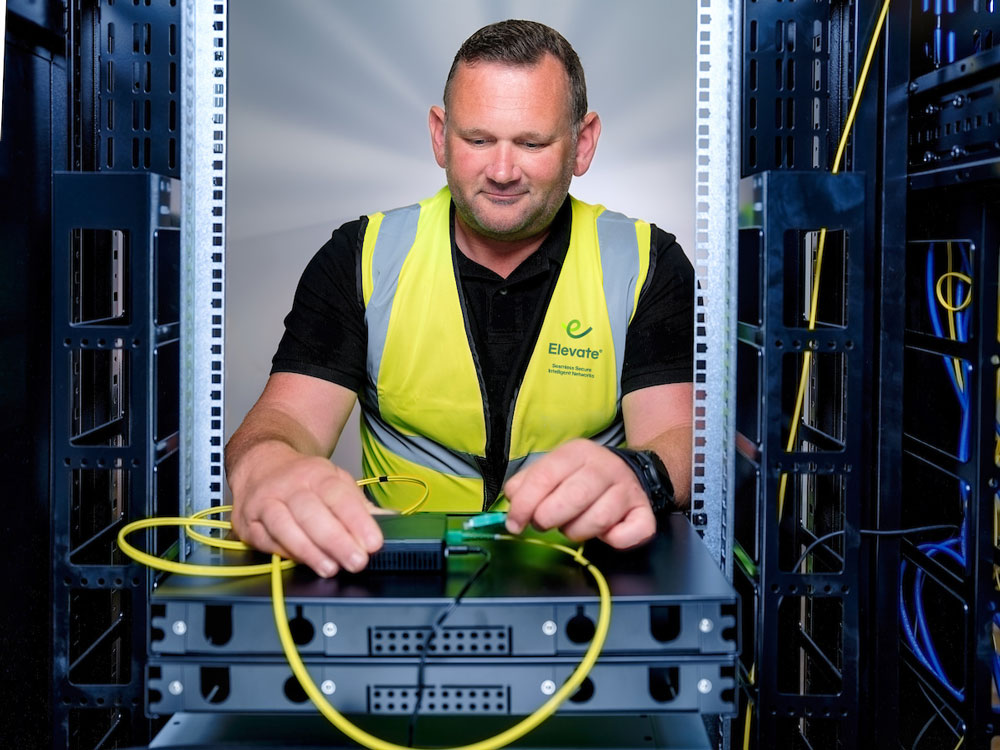 Technician in a yellow safety vest working with network cables inside a server rack.