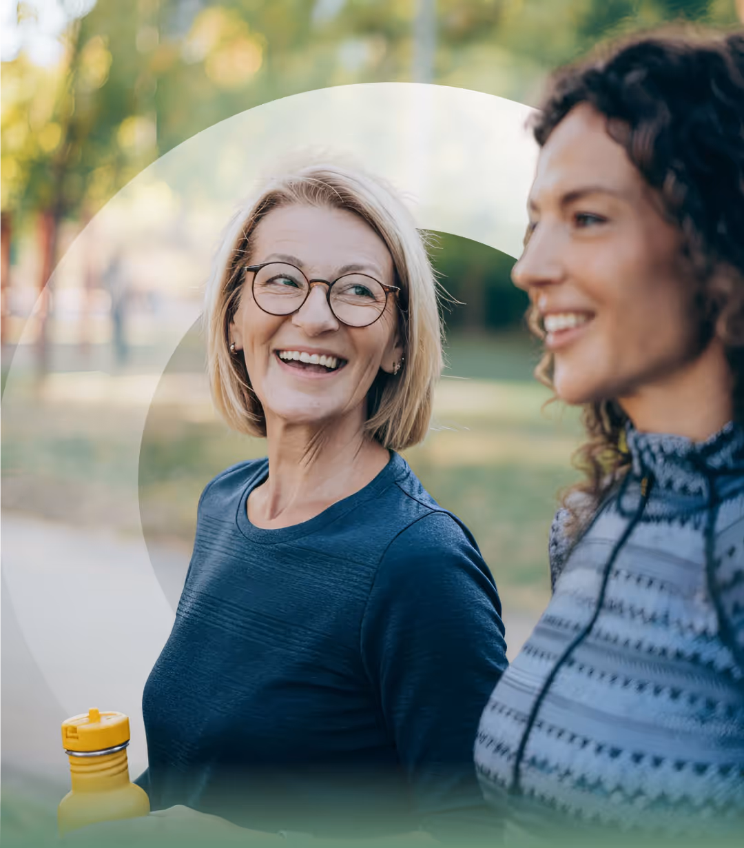 Two women walking outdoors and smiling, one holding a yellow water bottle.