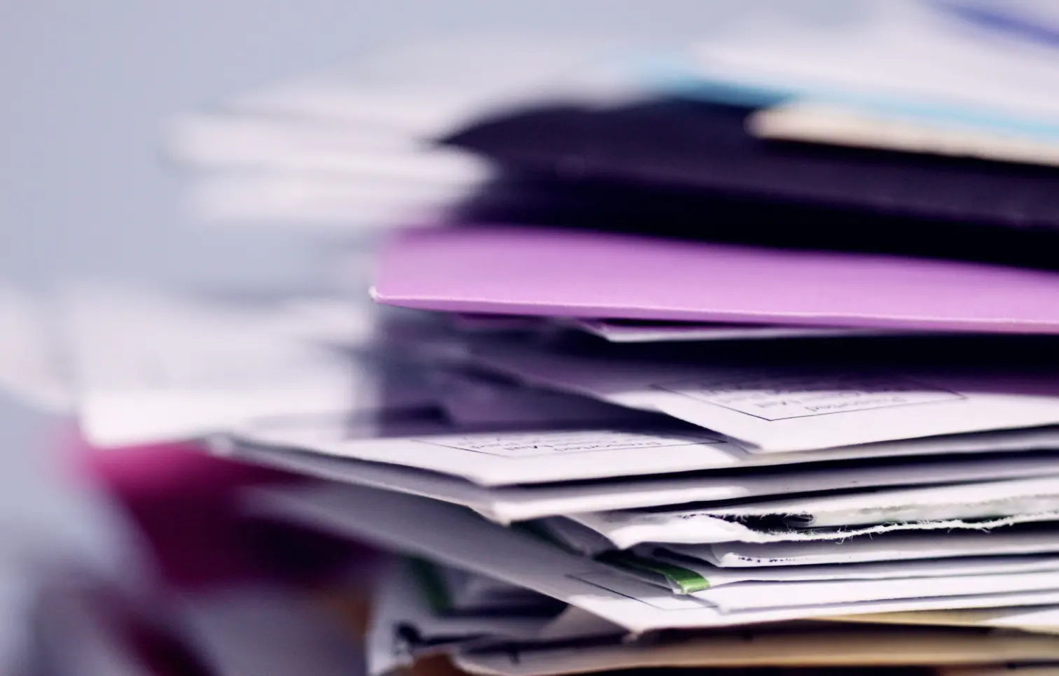 A high-angle, close-up photograph with a shallow depth of field showing a tall, disorganized stack of colorful paper files and documents. The image serves as a visual metaphor for the administrative documentation burden and "pajama time" that urologists fa