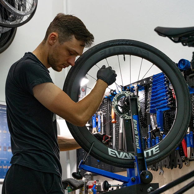 Mechanik rowerowy naprawia koło w serwisie rowerowym w Łomży, otoczony profesjonalnymi narzędziami warsztatowymi.