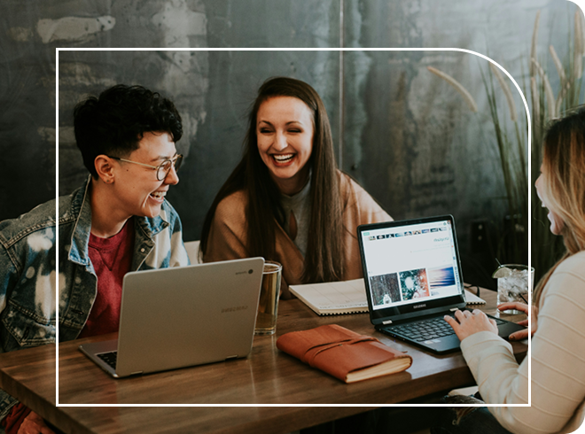 A group of young workers collaborating on a website whilst laughing behind their laptops
