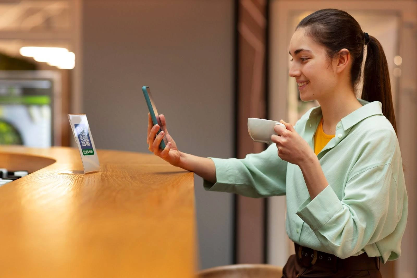 Woman scans QR code at counter while holding coffee cup