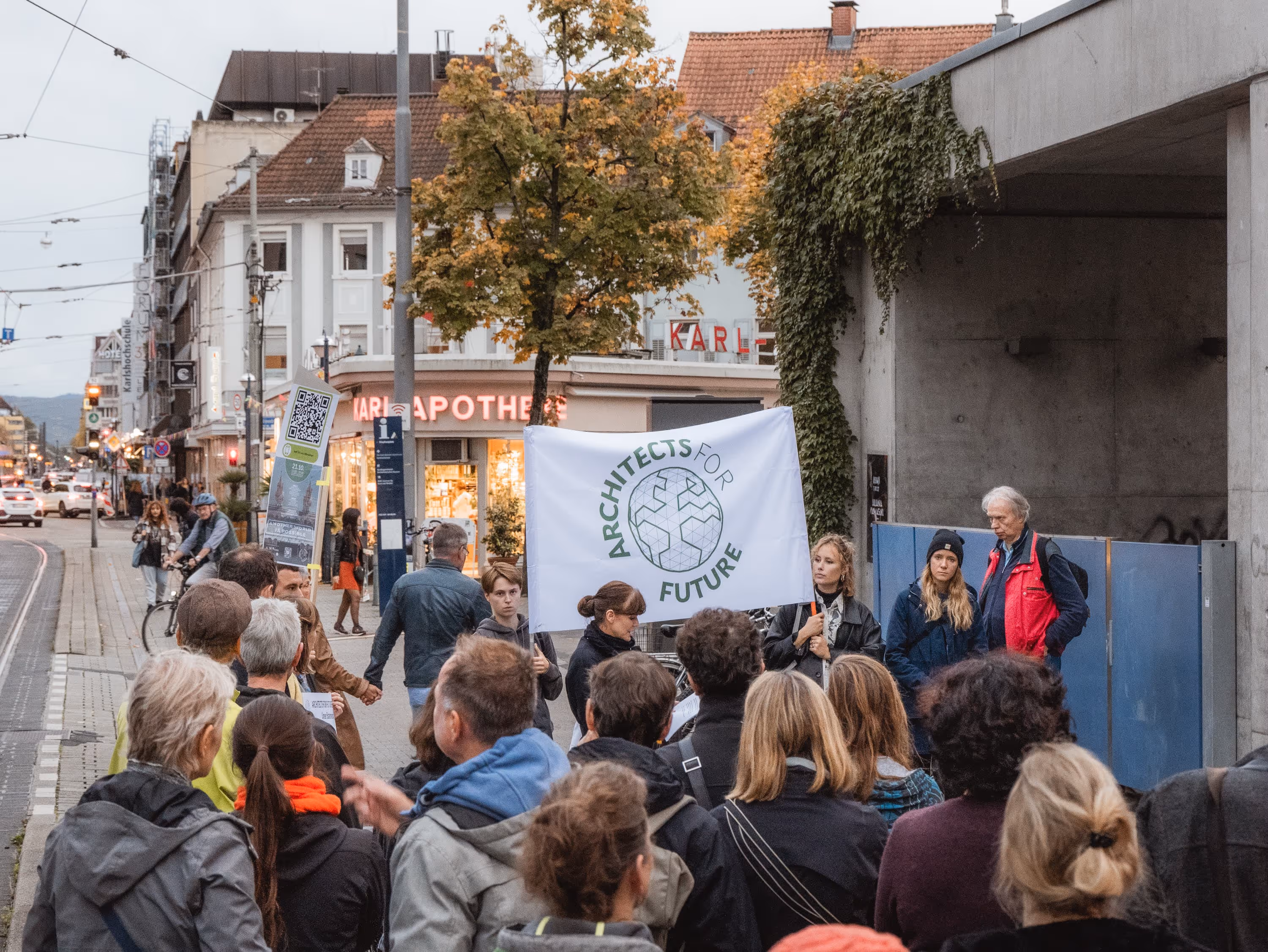 Gruppe von Menschen bei einer Demonstration in der Stadt, eine Person hält ein Banner mit der Aufschrift 'Architects for Future'.