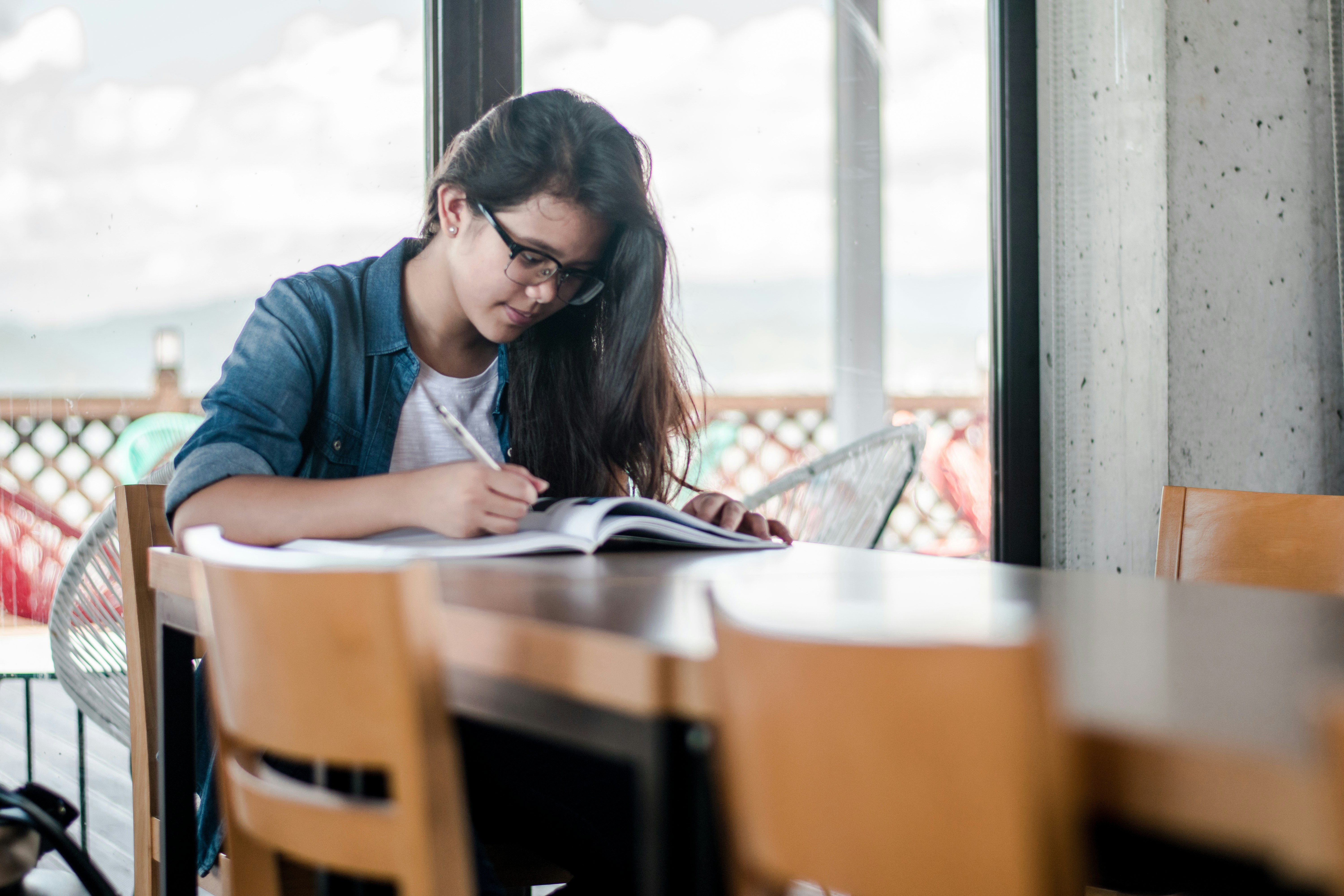 woman wearing glasses writingo n a wooden table  on paper on a woo